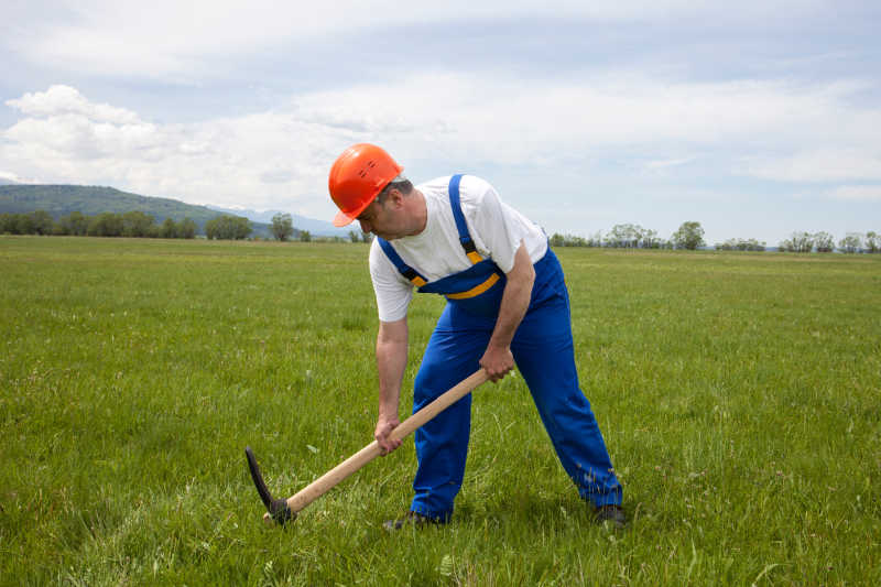 A worker digging up a field with a pickaxe