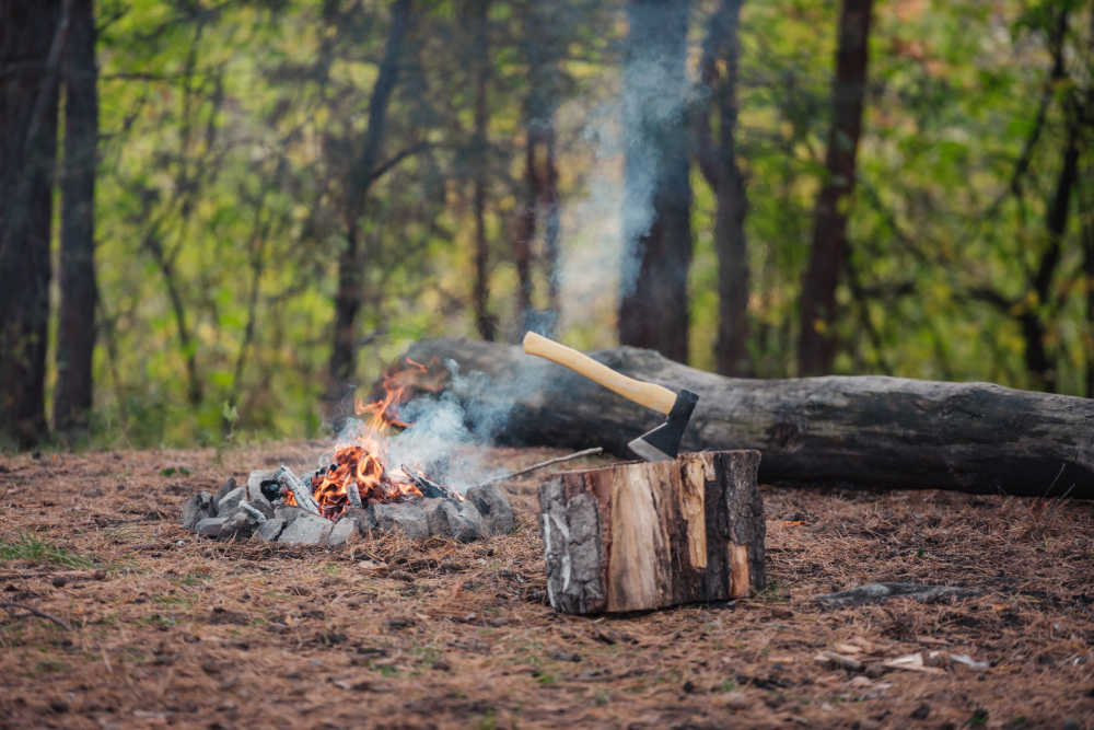 A camping axe in a wood stump next to a camp fire