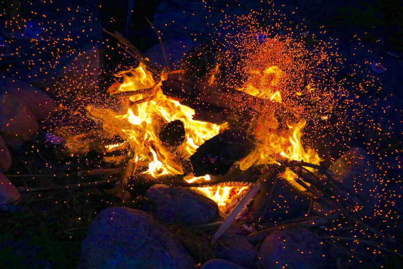 A flaming campfire giving off a lot of sparks.