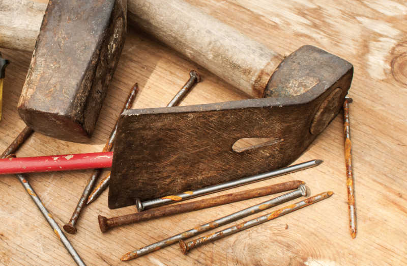 An adze lying on a work bench next to nails and a mallet