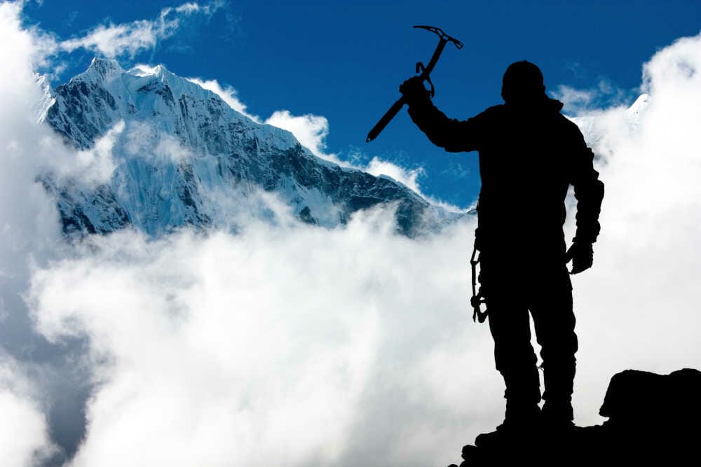 A mountaineer at the top of a peak holding an ice axe
