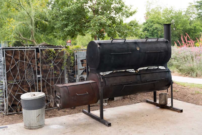 A large smoker with a wood stack in the background
