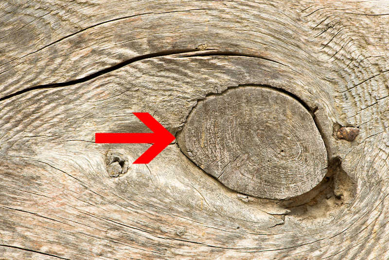 A closeup image of a knot in wood with an arrow pointing at it