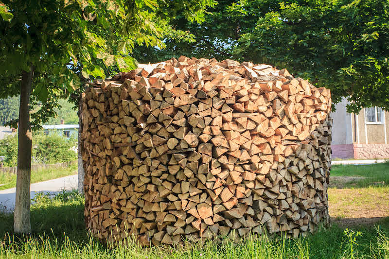 A circular wood stack near a house and tree