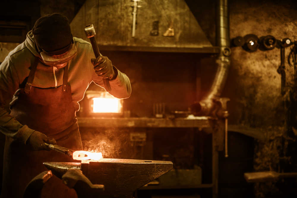 A metalsmith crafting an axe head using a hammer and anvil, and the hot forging method